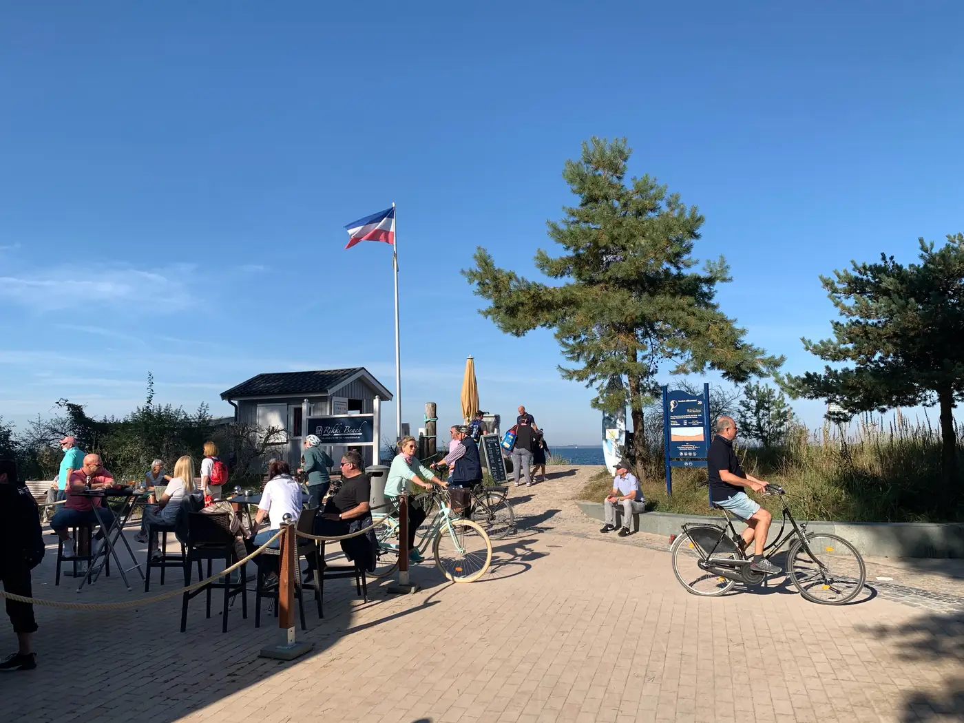 Menschen am Rikki-Beach-Strandbereich mit Hütte, Sitzplätzen und Weg zum Meer